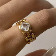 Gold ring with a large diamond on a person's finger against a neutral background